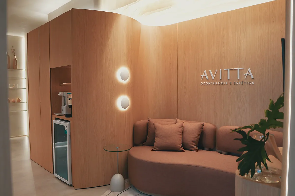 O lounge da Avitta, com o sofá curvo terracota e o logo na parede de madeira