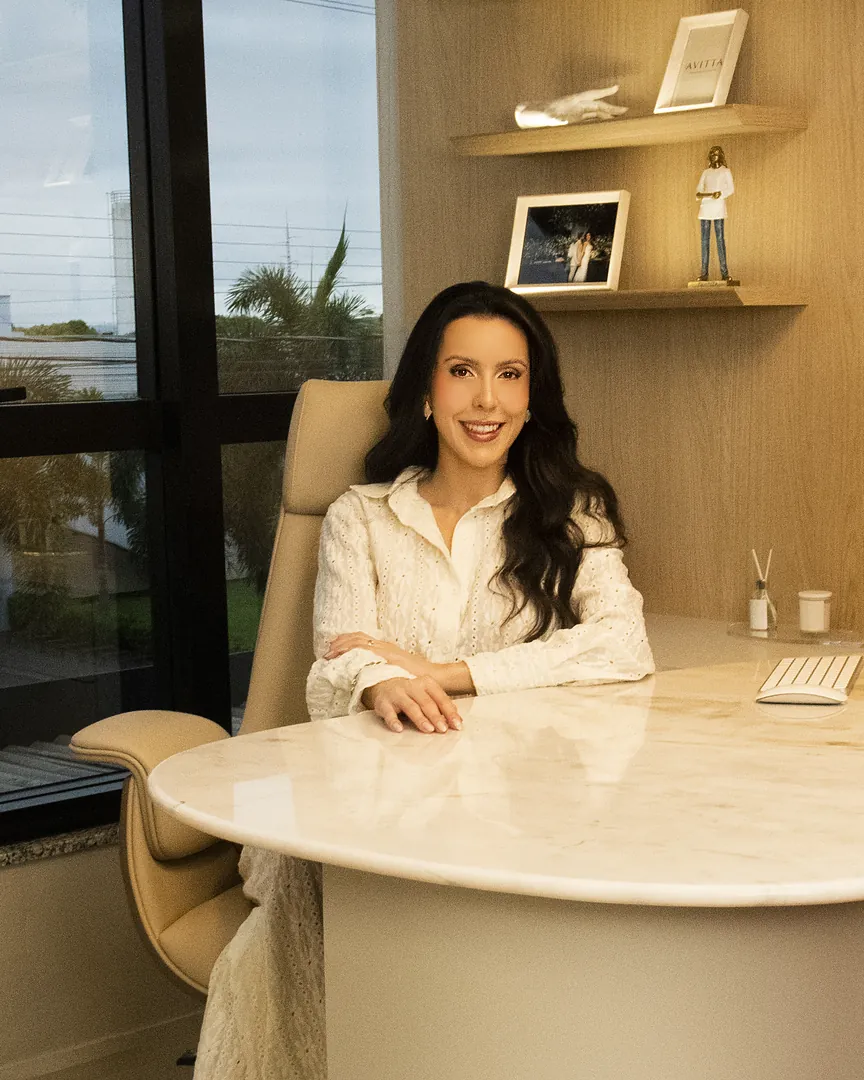 Dra. Bárbara Gasparin sorrindo, sentada à mesa do consultório na Avitta